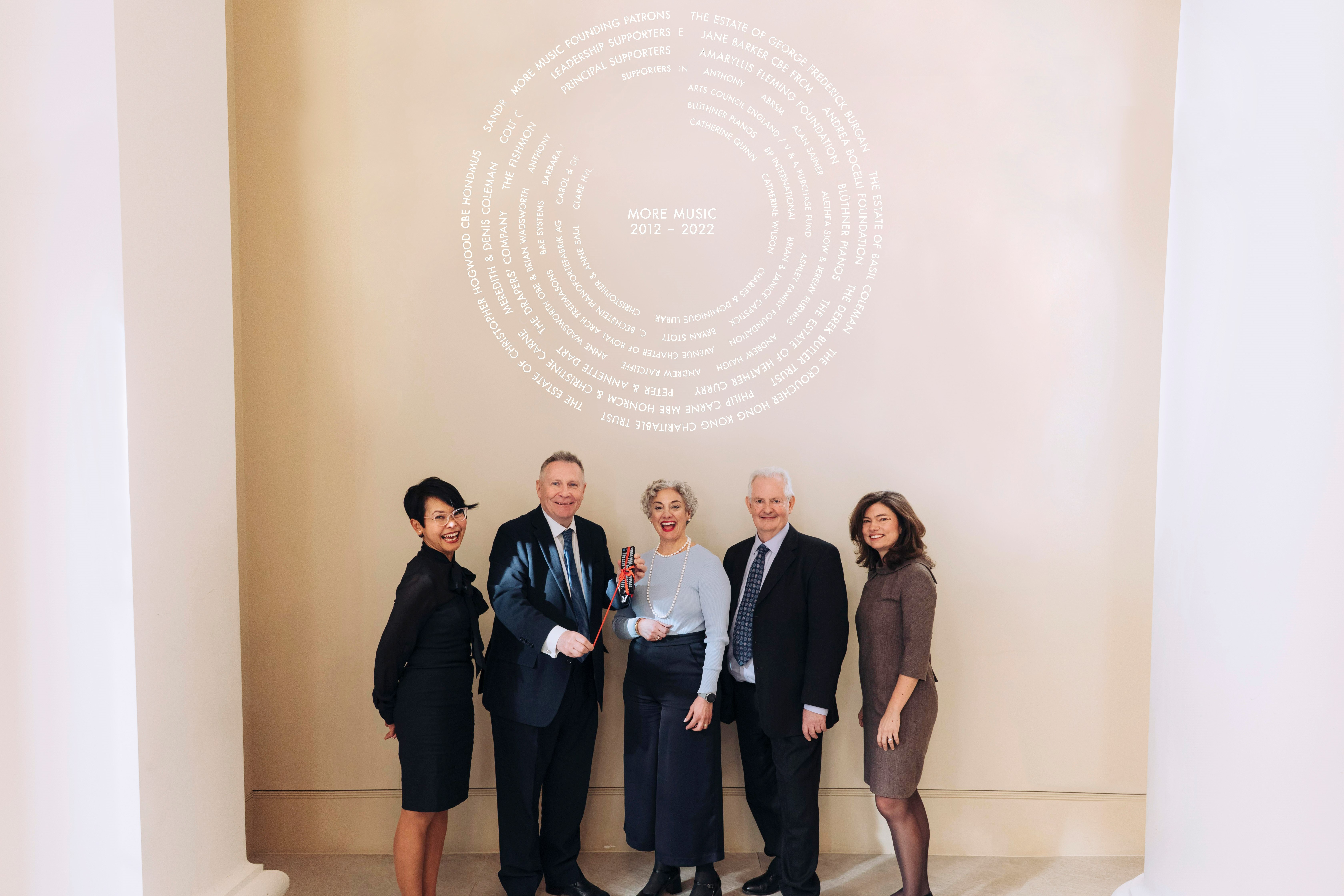 Members of staff stood in front of the new More Music Donor Recognition, a projection of names against a wall, of the RCM’s café.